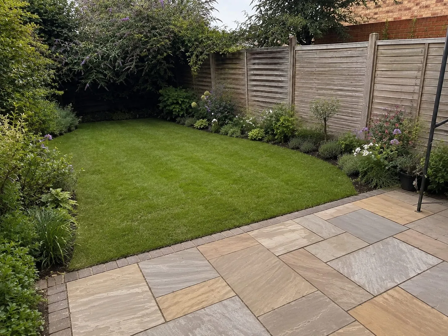 The same garden after Greenford's redesign, with a new striped lawn, planted borders and a clean sandstone patio.