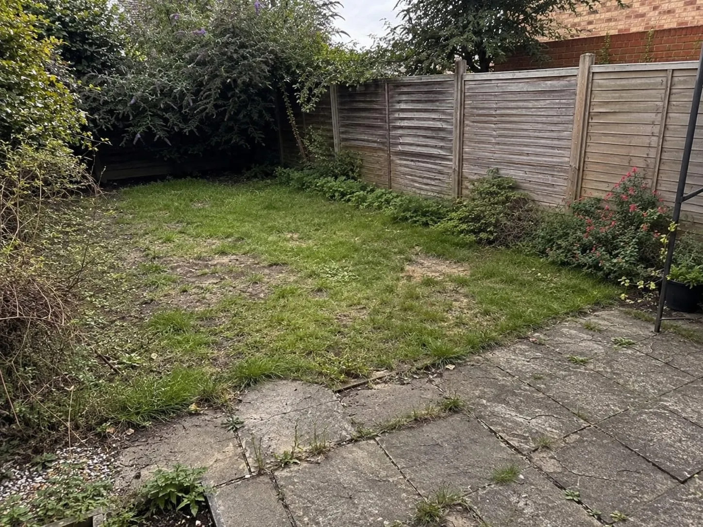 A tired Cardiff back garden before Greenford's work, with patchy lawn and mossy, cracked paving.