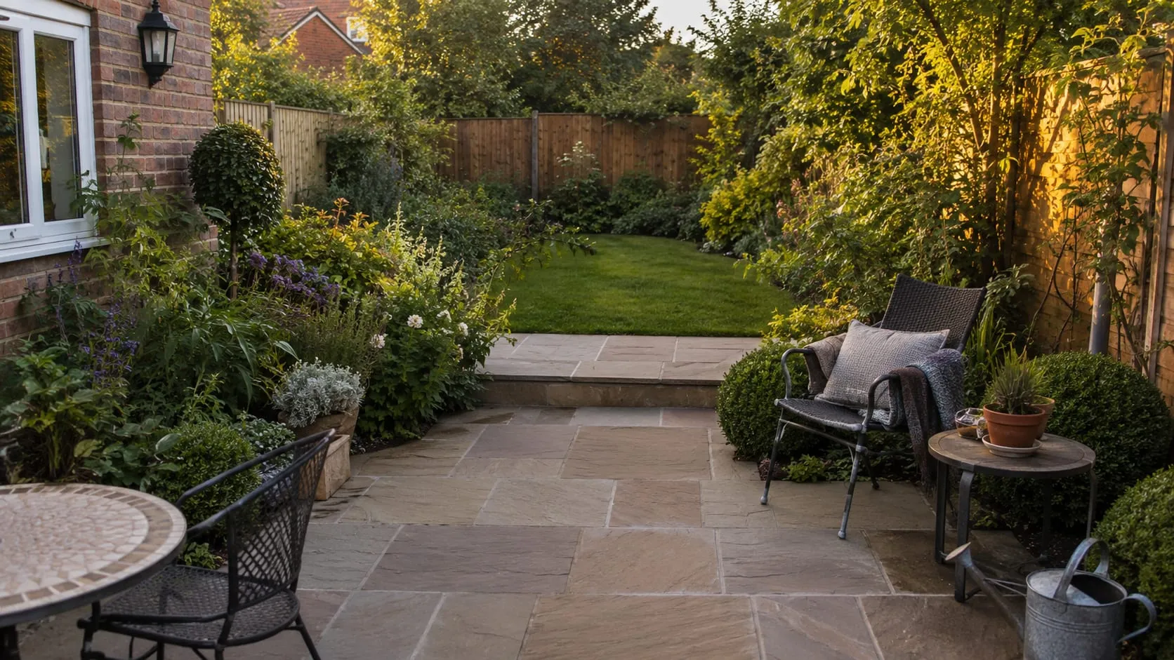 A finished Greenford garden at golden hour, with a natural stone patio and soft informal planting.